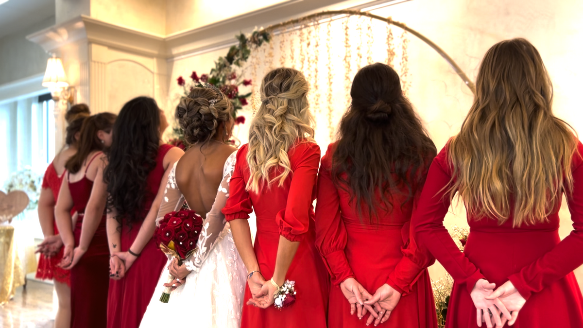 Bridesmaids in red dresses holding bouquets behind their backs at a wedding