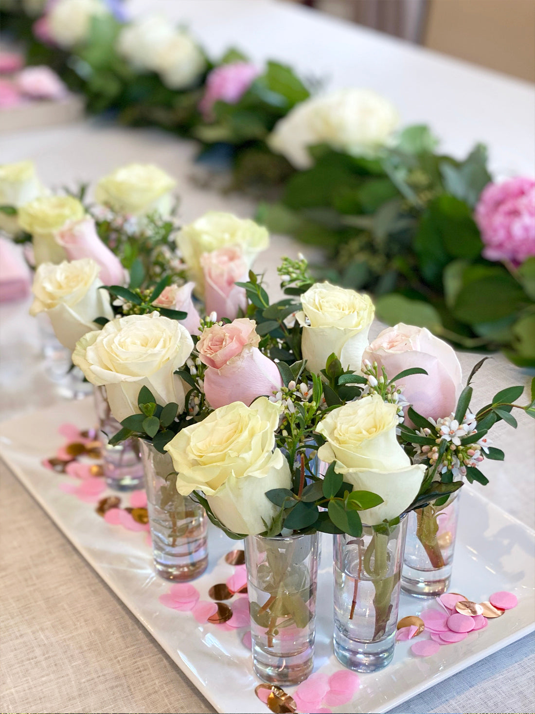 Baby shower table runner of white and pink roses in bud vases with greenery